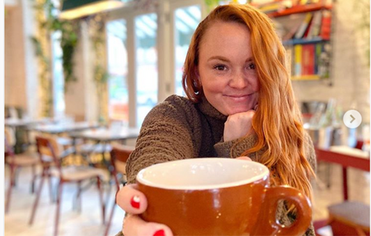 Woman enjoying coffee in a cozy cafe, smiling and holding a large brown mug.