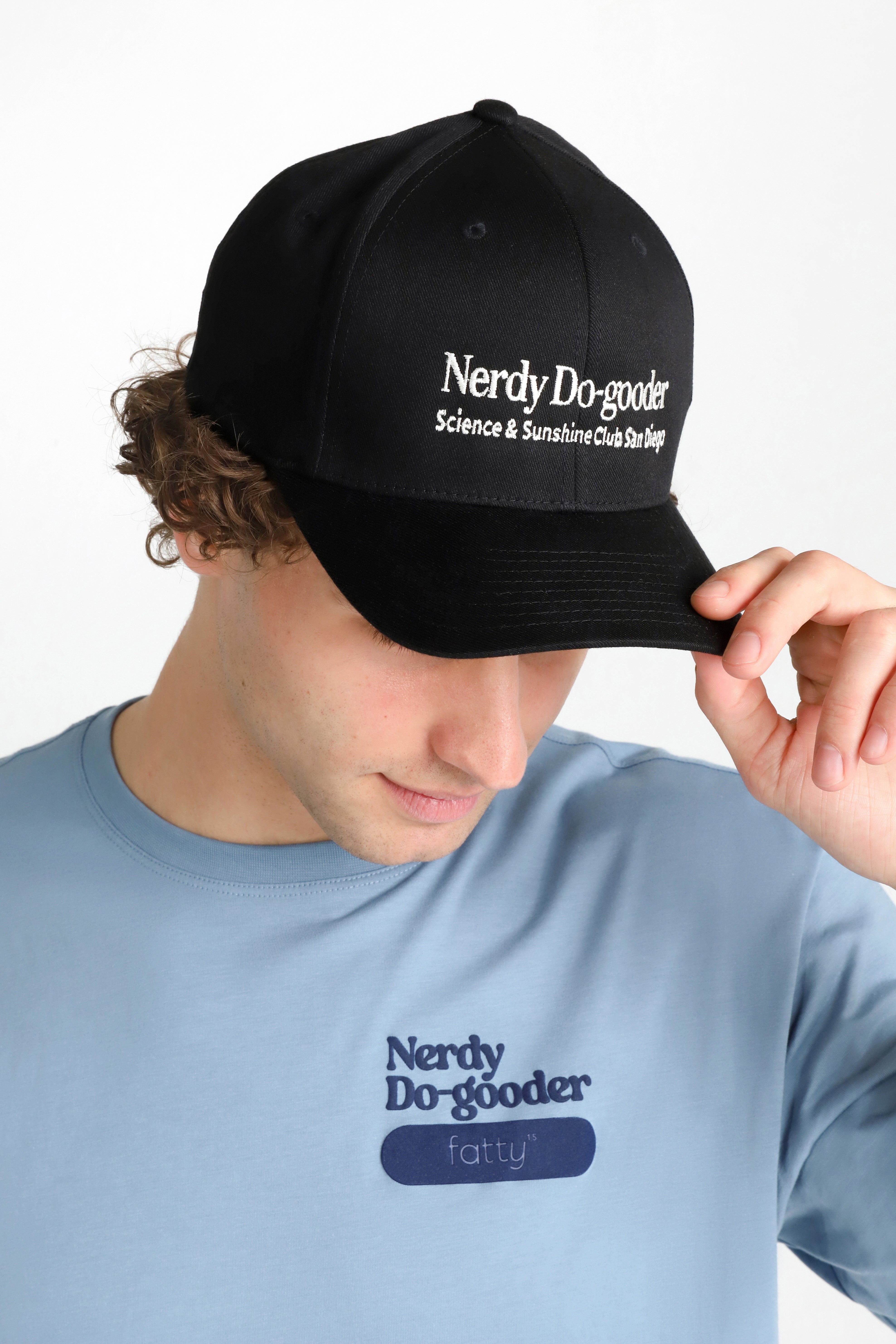 Man wearing a blue Nerdy Do-gooder T-shirt and black cap, looking down.