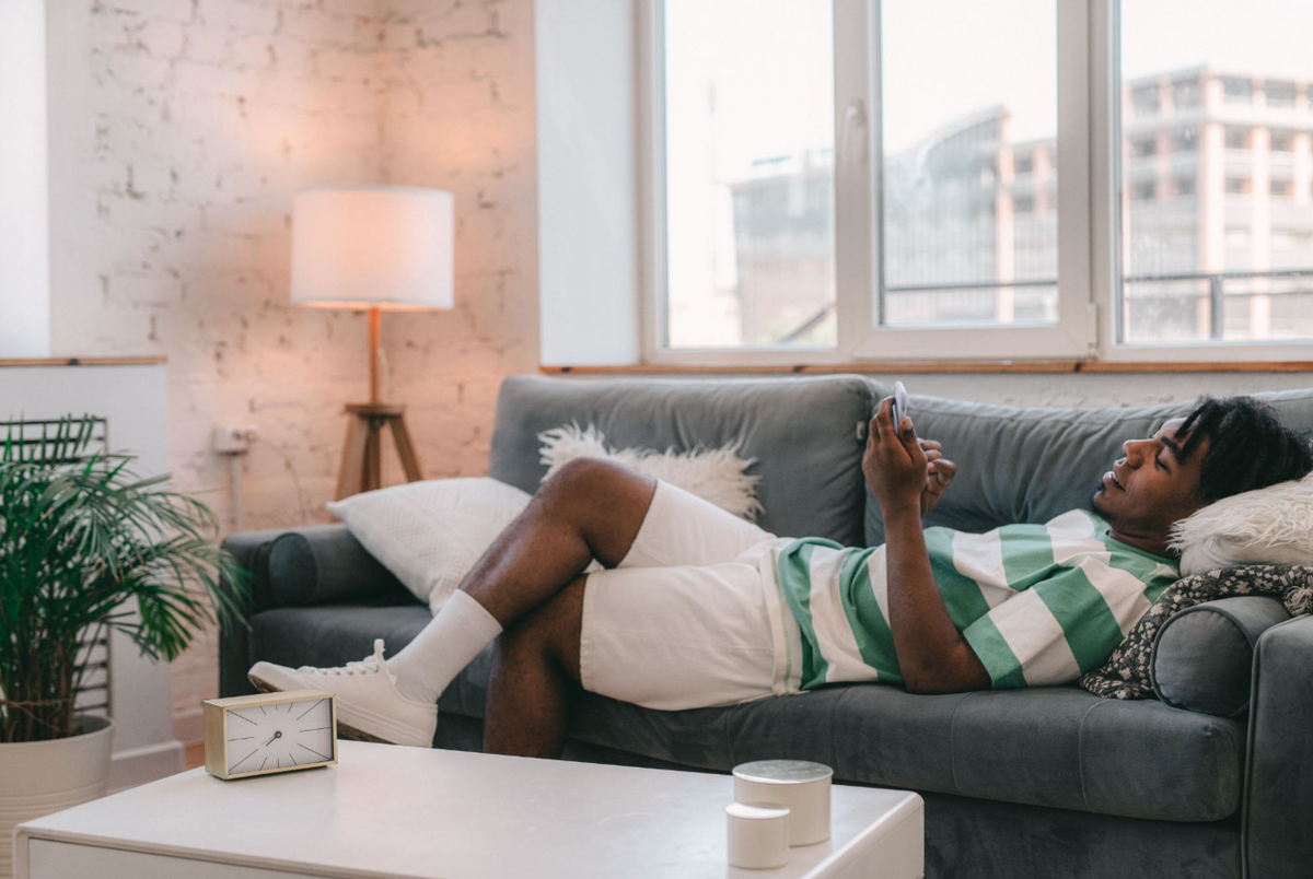 A person is lying on a grey couch while looking at their phone.