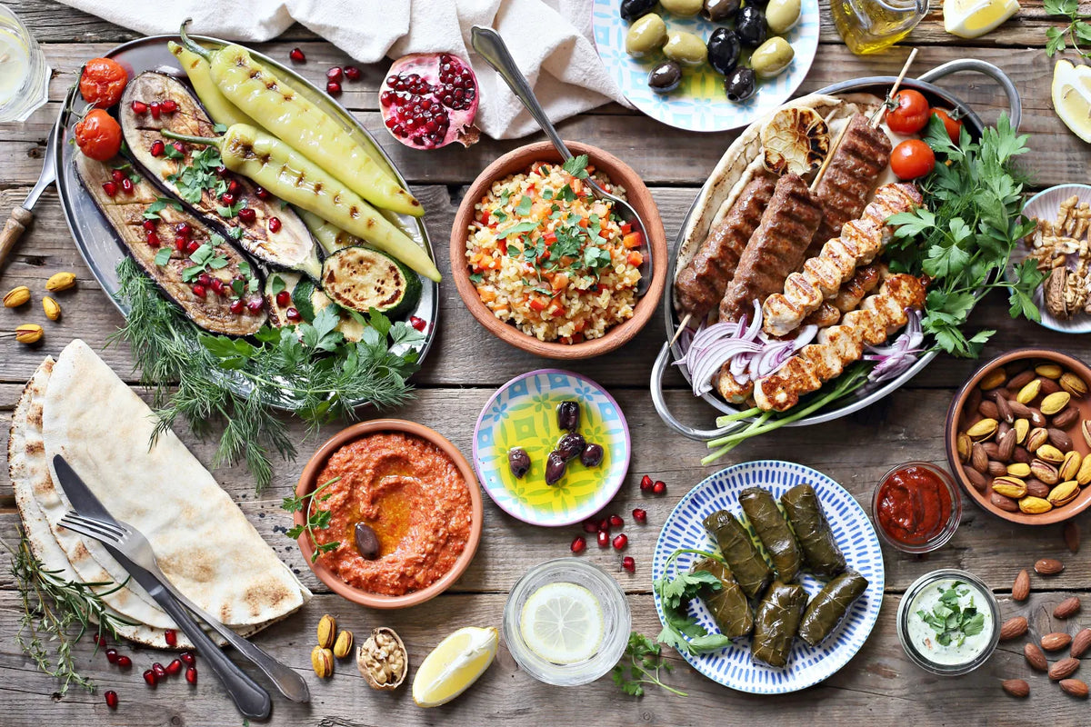 Mediterranean feast with grilled vegetables, kebabs, rice, and fresh herbs on a rustic table setting.