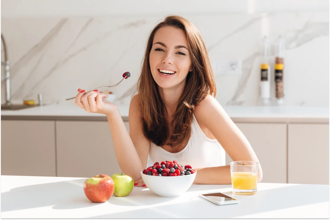 Smiling woman enjoying a healthy berry breakfast in a modern kitchen.