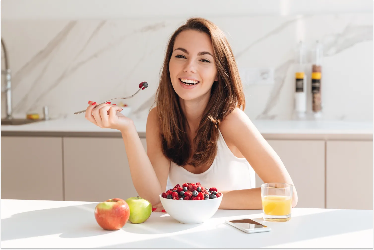 Smiling woman enjoying a healthy berry breakfast in a modern kitchen.