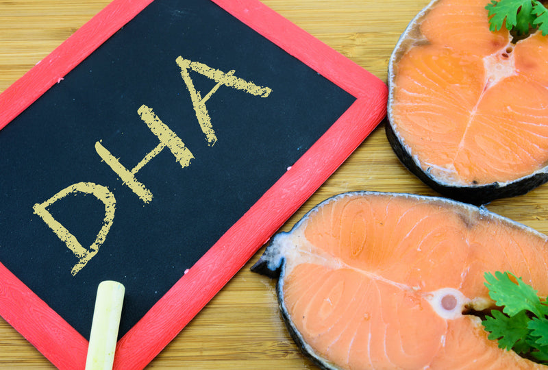 Salmon steaks next to DHA chalkboard sign on wooden surface.