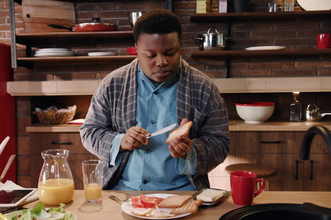 Man in a robe spreading butter on toast at a breakfast table with orange juice, tomatoes, and salad — illustrating the ongoing debate about whether butter is bad for you and its role in a balanced diet