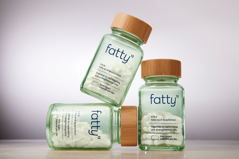 Three Fatty15's C15 supplement bottles on a reflective surface.