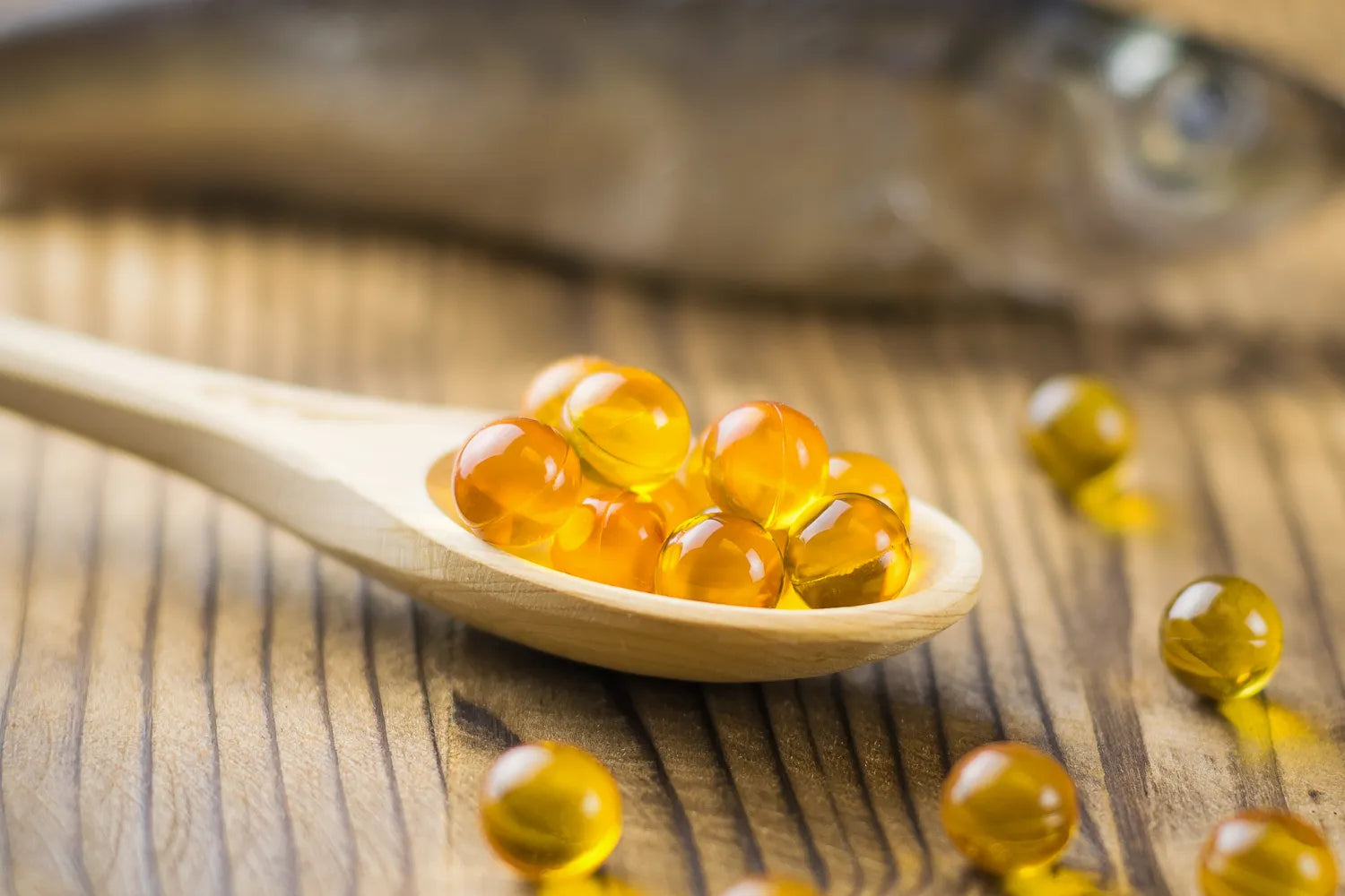 Wooden spoon with golden oil capsules on table.