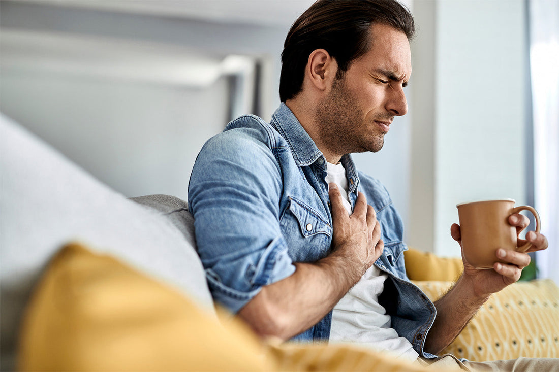 Man holding chest and cup, showing signs of discomfort.