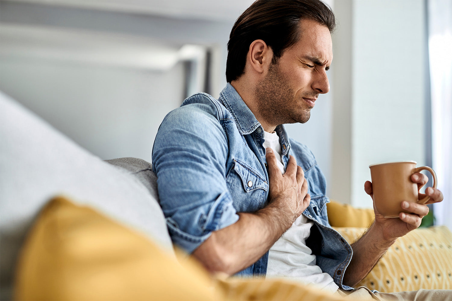 Man holding chest and cup, showing signs of discomfort.