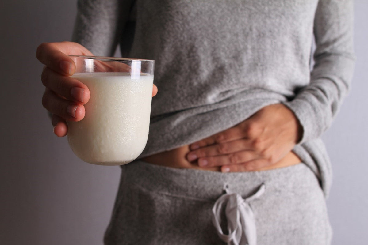 Person holding a glass of milk with hand on stomach, wearing gray clothes.