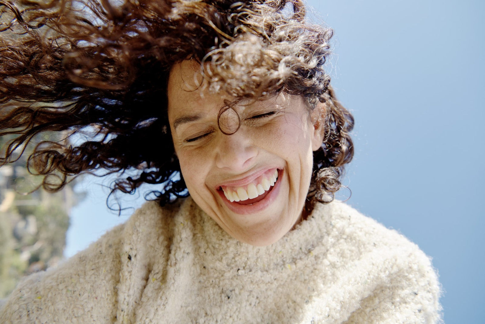 Smiling woman with curly hair enjoying a sunny day.