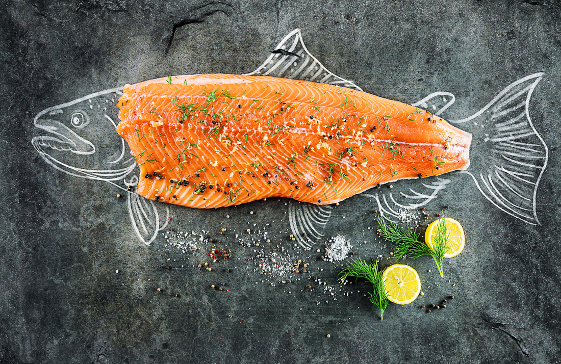 Fresh salmon fillet seasoned with herbs and pepper on a slate background.