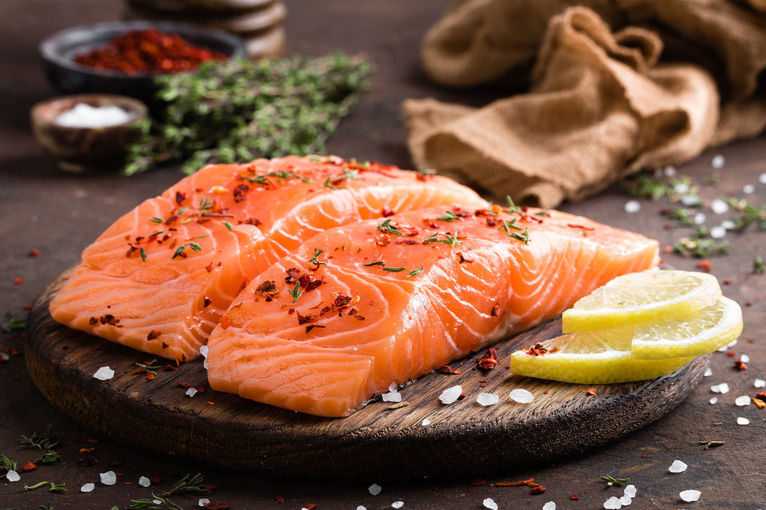 Fresh salmon fillets on wooden board with herbs and lemons.