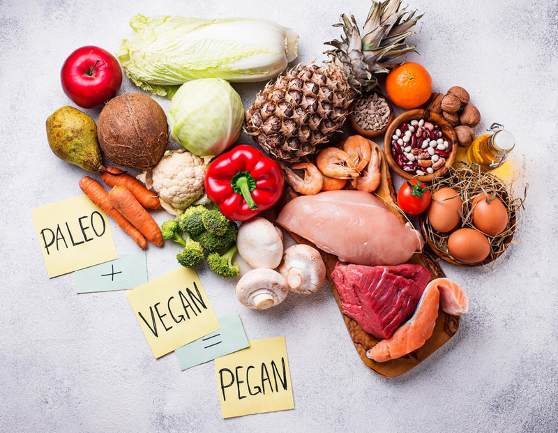 Pegan diet foods including fruits, vegetables, meats, and nuts arranged on a table with paleo and vegan sticky notes.