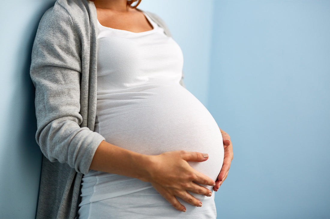 Pregnant woman holding belly in white shirt and gray cardigan.