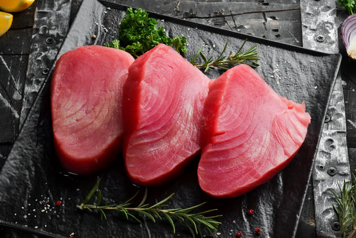 Fresh tuna steaks with rosemary and parsley on slate board.