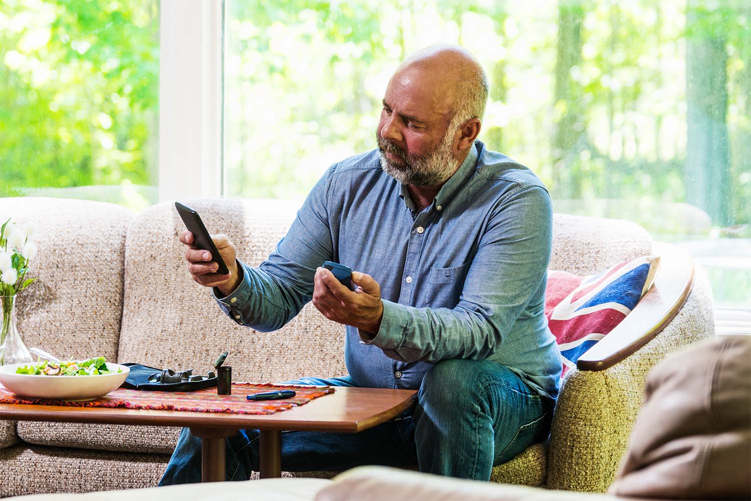 Man checking blood sugar at home while eating salad.