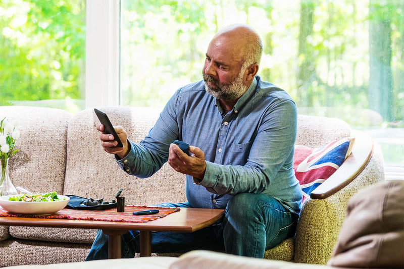 Man checking blood sugar at home while eating salad.