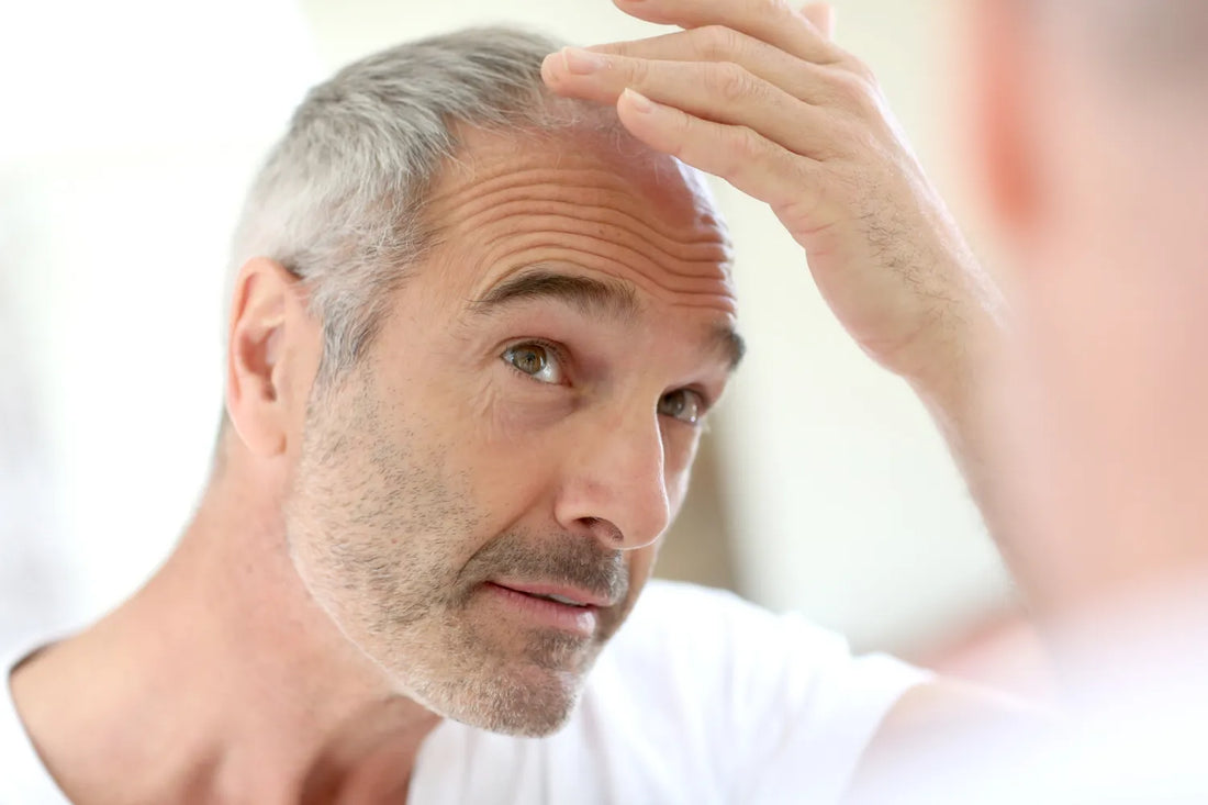 Man examining hair in mirror, looking concerned about hair loss.