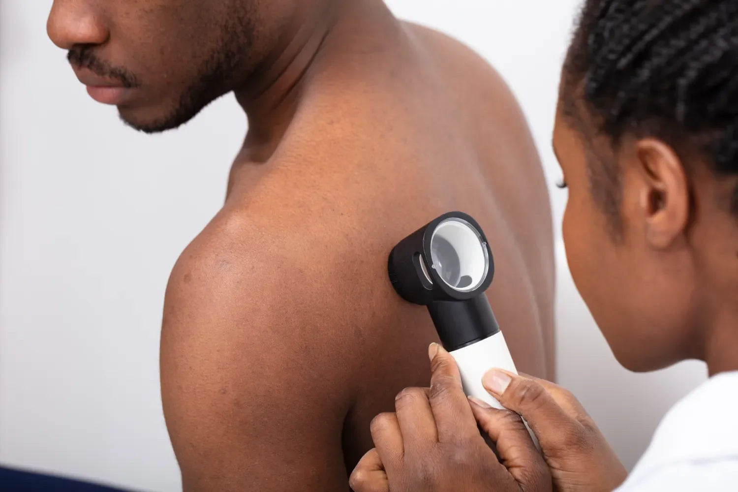 Doctor examining skin with dermatoscope on patient's back.
