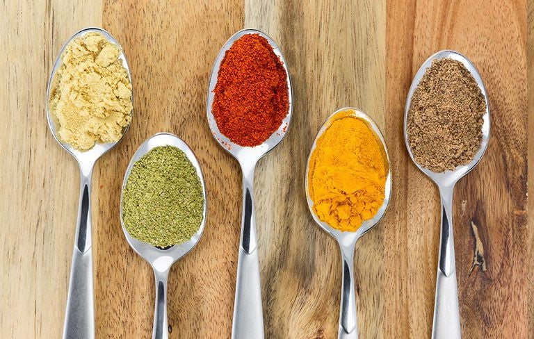 Five spoons of colorful spices on a wooden table.