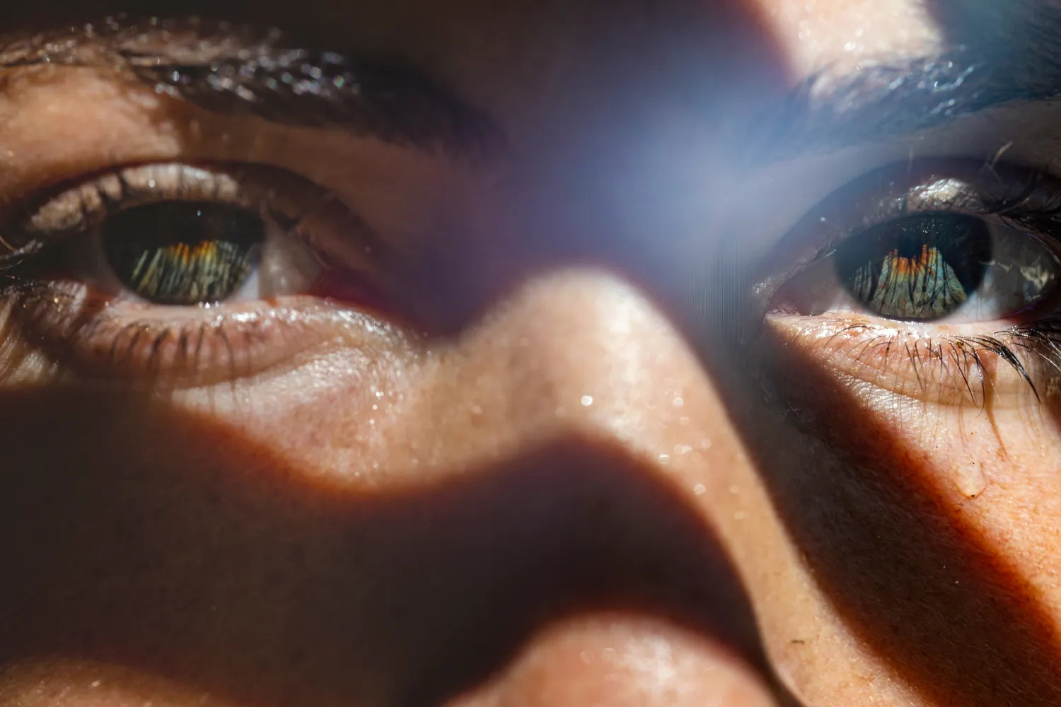 Close-up of eyes with sunlight shadow pattern on skin.
