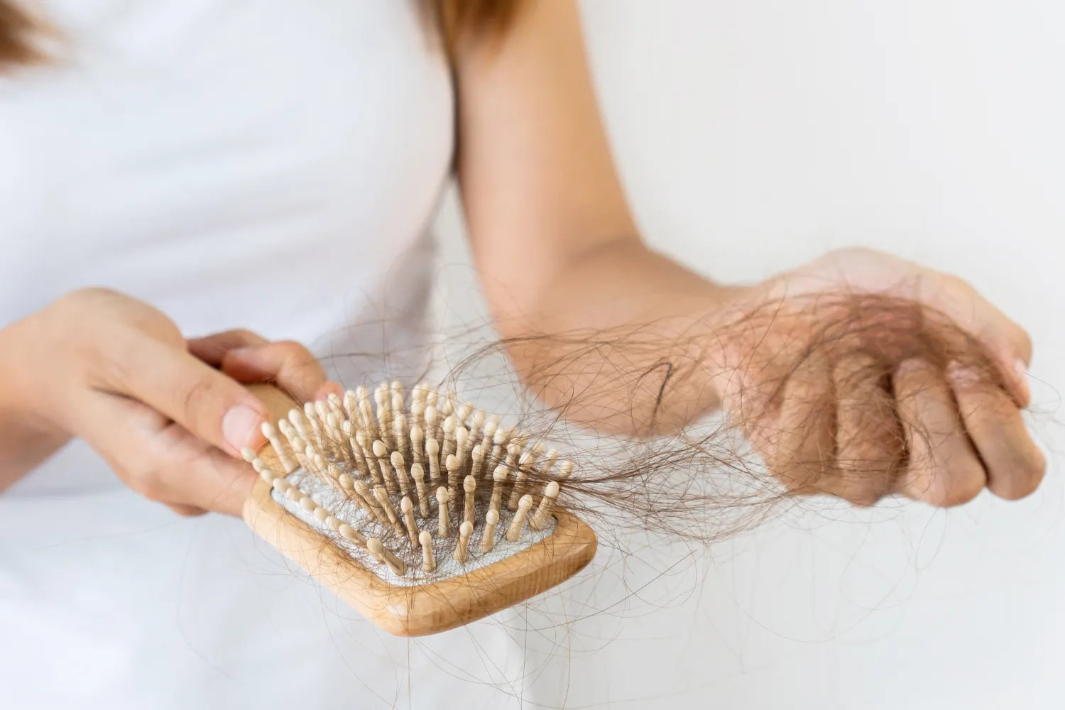 Person holding hairbrush with hair, experiencing hair loss.