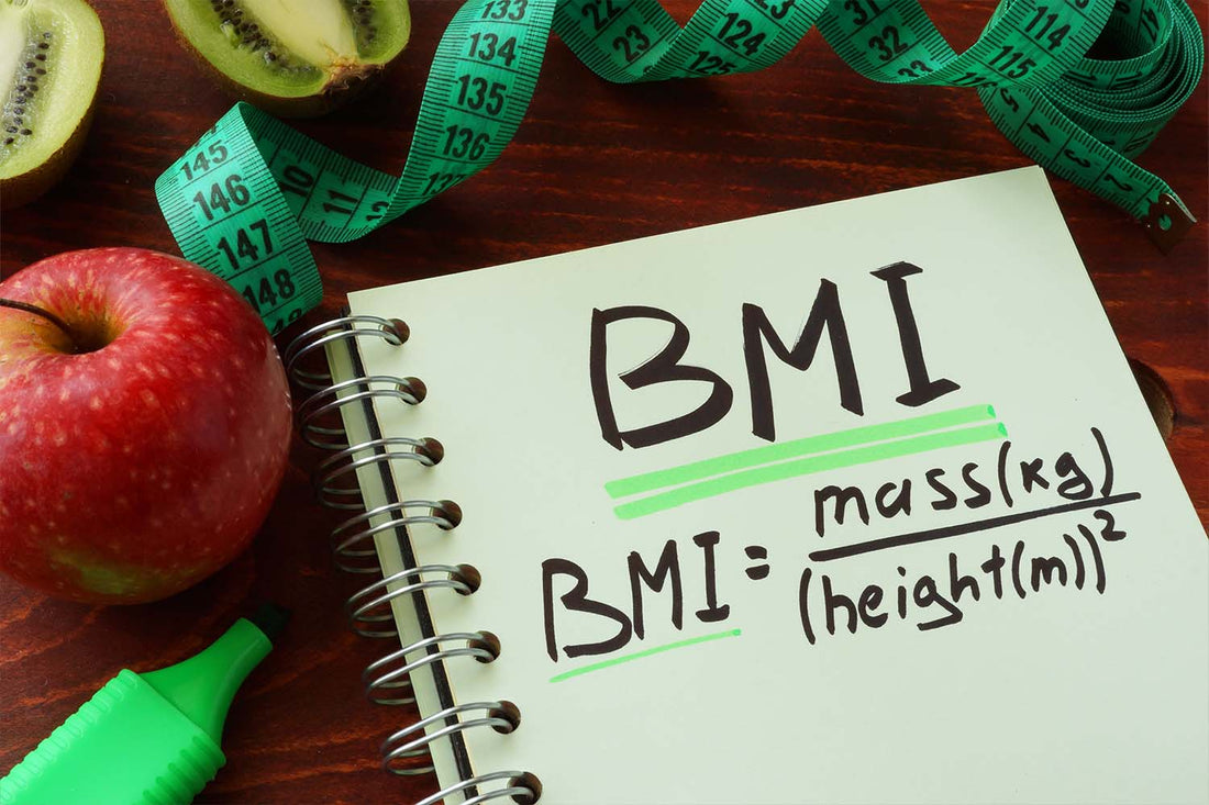 Notebook with BMI formula, apple, kiwi, and measuring tape.