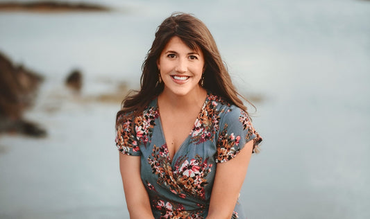 Woman smiling by the water in a floral dress.