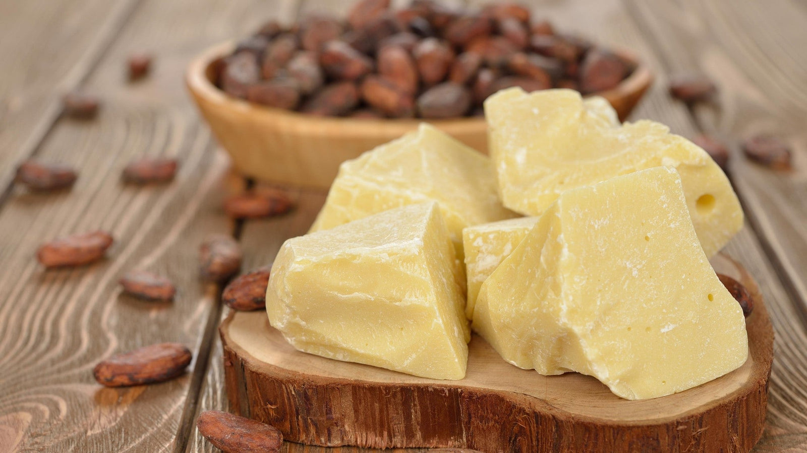 Cocoa butter chunks with cocoa beans on rustic table.