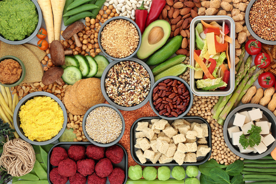 Variety of plant-based foods including nuts, seeds, grains, and vegetables displayed in bowls.