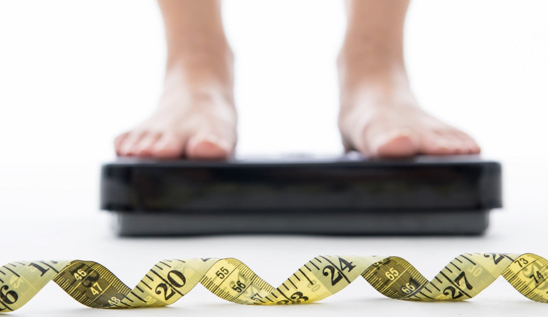 Person standing on a scale with a yellow measuring tape in focus.