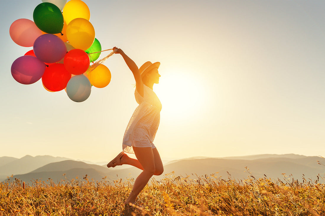 Woman joyfully running with colorful balloons at sunset.