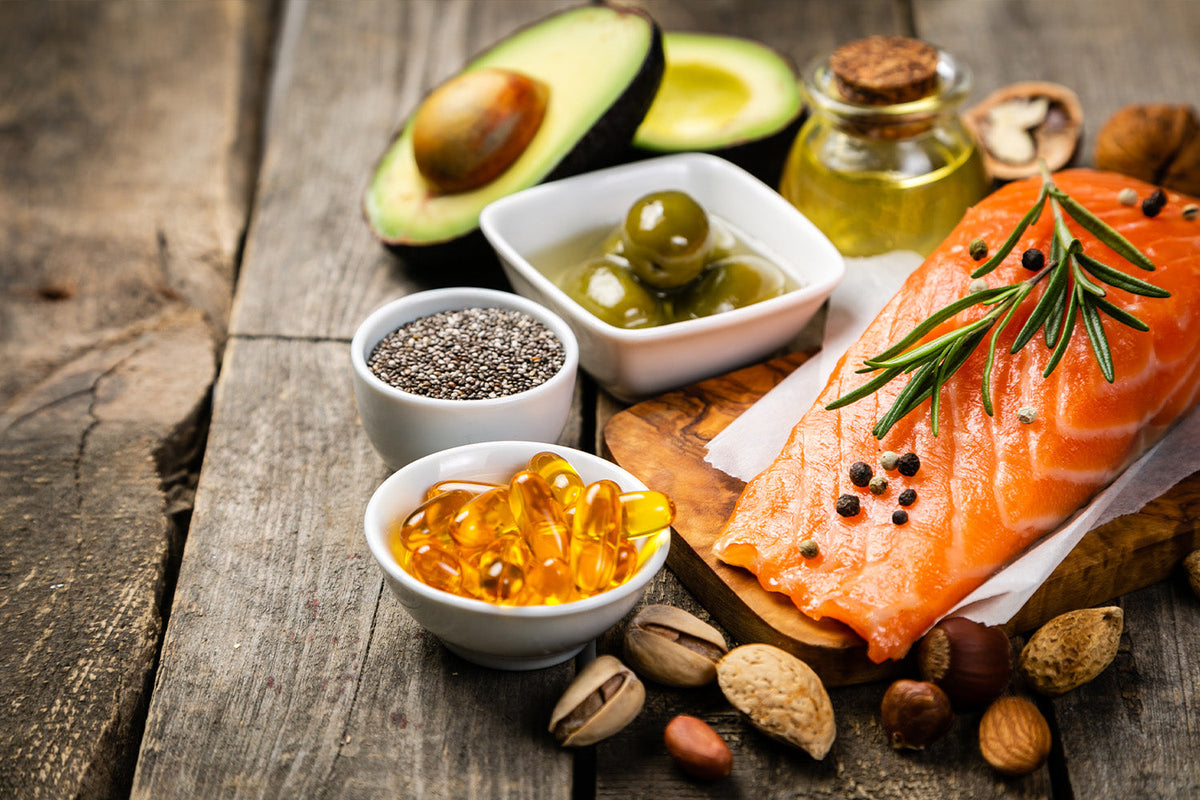 Salmon with avocados, olives, nuts, chia seeds, and fish oil capsules on a wooden board.