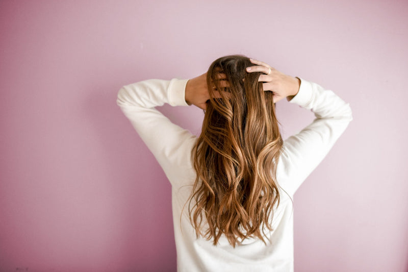 Woman with long, wavy hair against pink background.