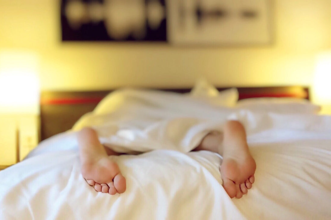 Cozy feet under white duvet in warm bedroom setting.