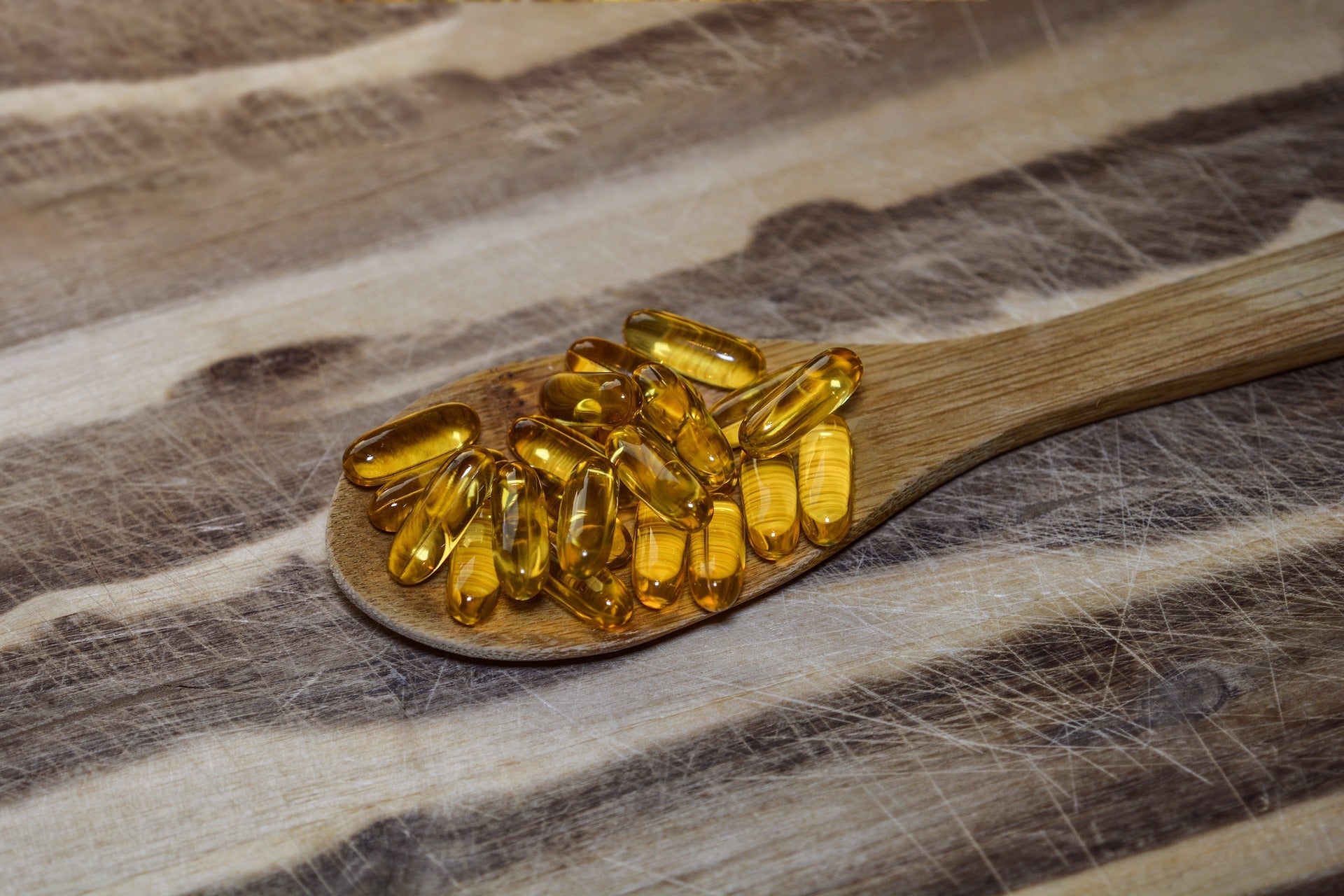 Wooden spoon with yellow oil capsules on a rustic table.