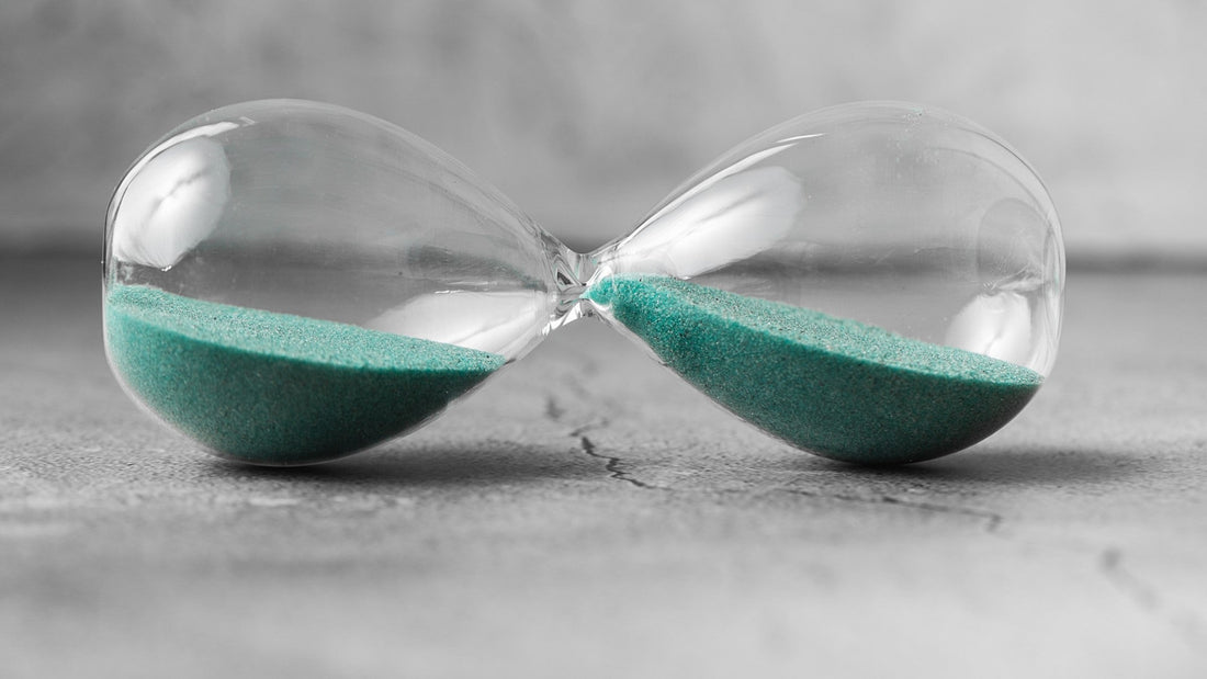Hourglass with green sand lying on textured surface, symbolizing passage of time.
