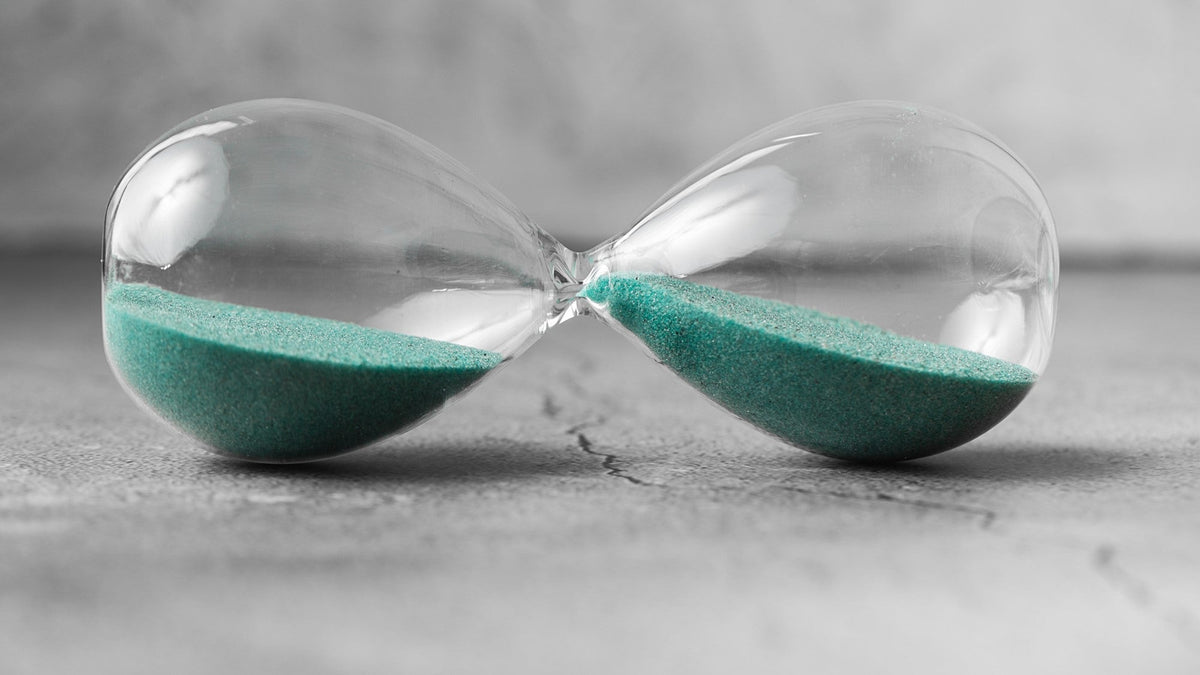 Hourglass with green sand lying on textured surface, symbolizing passage of time.