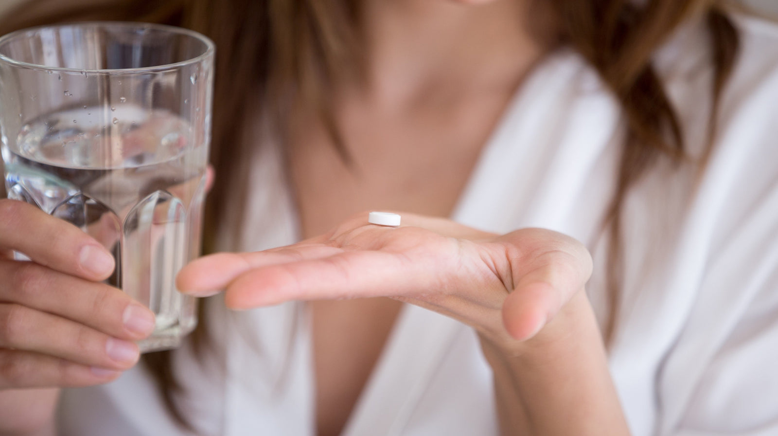 Person holding tablet and glass of water, preparing to take a supplement.