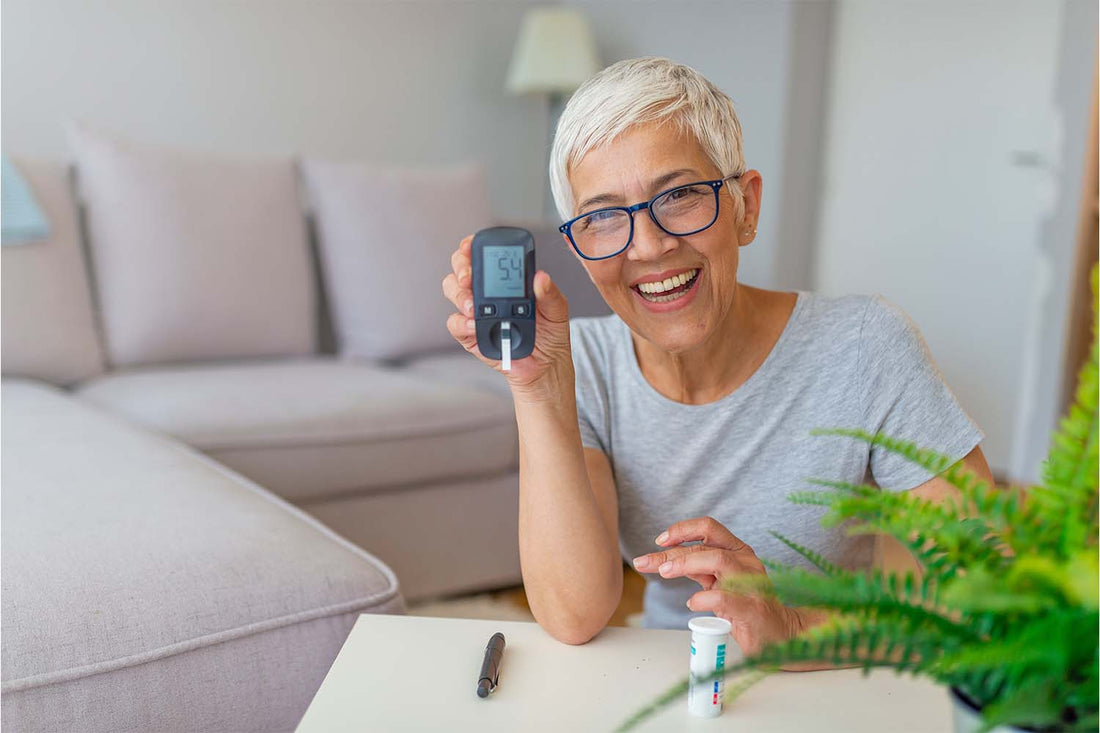 Elderly woman smiling while holding a glucose meter in a cozy living room.