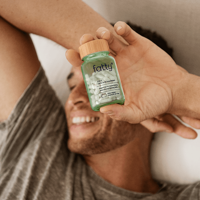 Man smiling while holding Fatty15's C15 supplement in bed.