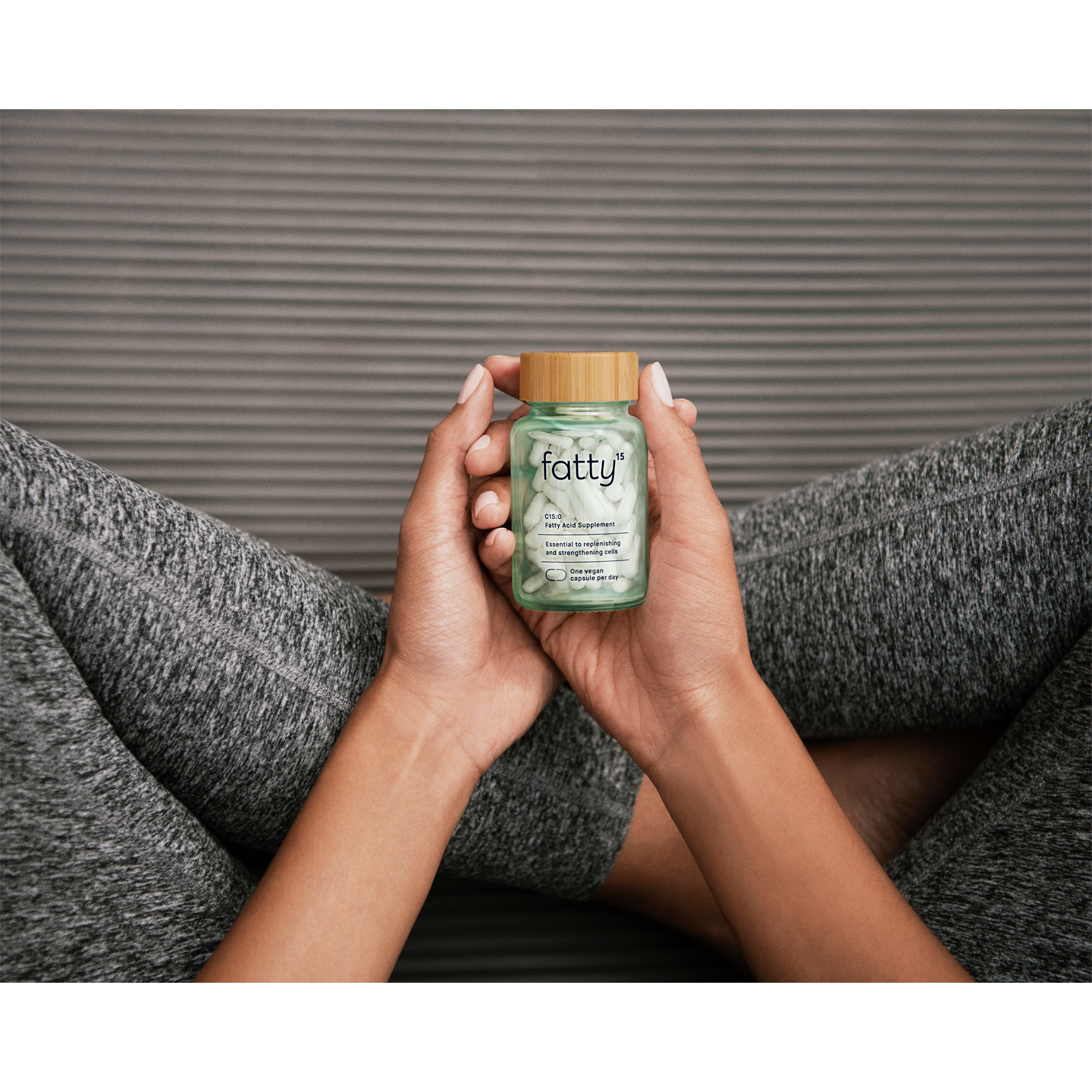 Person holding Fatty15's C15 supplement bottle while seated on yoga mat.