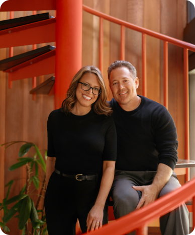 Man and woman smiling on a red staircase indoors.
