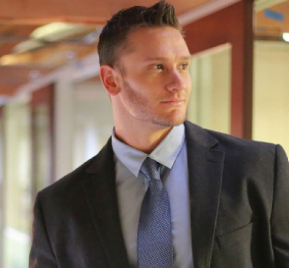 Business professional in a suit and tie standing in an office hallway.